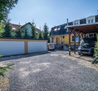 A parking lot in front of the guesthouse with garages in Poprad surrounded by coniferous trees.