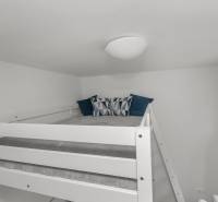 A bed on an elevated spot in a studio apartment with pillows and a blue curtain.