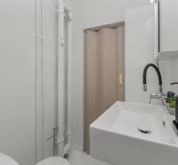 Compact bathroom in a studio apartment with a sink, faucet, and sliding doors.