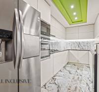 A kitchen in a family house with white cabinets, a marble backsplash, and a stainless steel refrigerator.