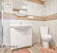 A bathroom in a family house with a sink, shower, and a floor with a wooden decor.