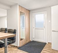Entrance area in a family house with a refrigerator, mirror, chairs, and a wooden-patterned floor.