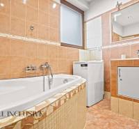 A bathroom in a family house with a bathtub, a washing machine, and tiles in warm colors.
