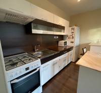 A kitchen in a one-room apartment with a wooden decor floor, a kitchen unit, and a gas stove.