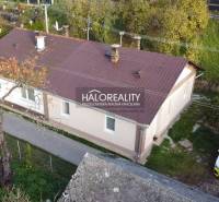 A family house in Sirk with a metal roof, surrounded by a green garden and a car in the yard.