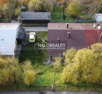 A family house in Sirk with a metal roof, a car in the parking lot, and surrounding trees.