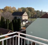 The view from the 3-room apartment in Tomášikovo shows gardens and an old building.