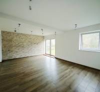A spacious living room with a stoneware wall and a wooden decor floor in a family house.