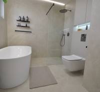 Bathroom in a family house with a bathtub, shower, and toilet, beige tiles.