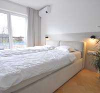 Bedroom in a family house with a bed, plant, and wooden decor flooring.
