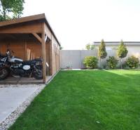 The garden of a family house on Ďuríčkova Street in Miloslavov with a wooden shelter and a motorcycle.