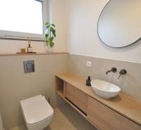 A bathroom in a family house with a round mirror, a sink, and a floor with a wooden decor.