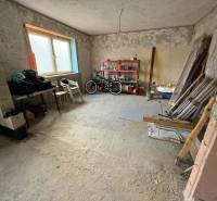 Unplastered room in a family house used as a workshop with stored items and bicycles.