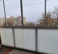 A glazed balcony in a 3-room apartment with a view of apartment buildings and trees.