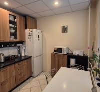 A kitchen in a 3-room apartment with white appliances, a wooden decor floor, and windows with blinds.