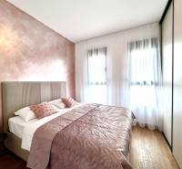 A bedroom in a one-room apartment with pink walls and a wood-patterned floor.