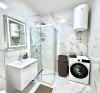 Bathroom in a studio apartment with a shower, washing machine, and elegant marble tiles.