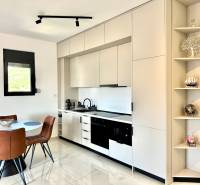 A kitchen in a studio apartment with a table, leather chairs, and white cabinets.