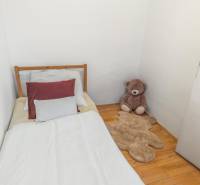A bed with pillows, a plush teddy bear, and a bear-shaped rug on a floor with wooden decor.