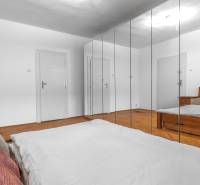 Bedroom in a 3-room apartment with wood-patterned flooring, mirrored wardrobes, and a bed.