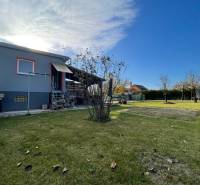 A cottage in the New Settlement in Komárno with a lawn, trees, and a clear blue sky.