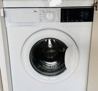 Built-in washing machine in a studio apartment with a wooden decor floor.