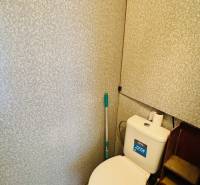 A toilet in a one-room apartment with a tank and a wall with a relief pattern.