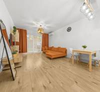 Living room in a two-room apartment with wood decor flooring, an orange sofa, and a dining table.