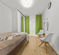 A bright room in a 2-room apartment with a bed, green curtains, and a wooden decor floor.