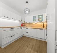 A kitchen with white cabinets, wooden countertops, and a wood-patterned floor in a two-room apartment.