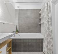 A bathroom in a 2-room apartment with a bathtub, sink, and shower curtain in neutral colors.