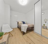 Bedroom in a 2-room apartment with wood-patterned flooring, a white chair, and a wardrobe.