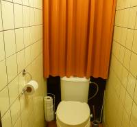 A toilet with an orange curtain and light tiles in a 2-room apartment.