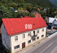 A building in Belá with a red roof on the main street surrounded by greenery and houses.