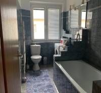 A bathroom in a 2-room apartment with blue tiles, a bathtub, and a sink.