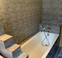 A bathroom in a 2-room apartment with a bathtub and marble tile cladding.
