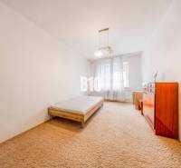 A bedroom in a 4-room apartment with a bed, a dresser, and a carpet.