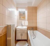 A bathroom in a 4-room apartment with a bathtub, light tiles, and a radiator.
