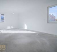 An empty room in a three-room apartment with light walls and large windows, without flooring with a wooden decor.