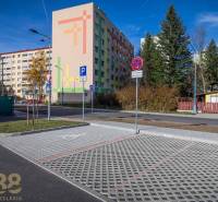 Exterior with an apartment building and a parking lot in Poprad, greenery and houses in the background.