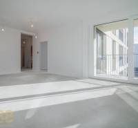 A room in a 3-room apartment with a large window, wooden decor flooring, white walls.