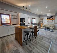 A family house with a wooden decor floor, a kitchen, and a living room equipped with comfortable seating.