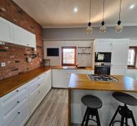 A kitchen with a brick wall, white cabinets, wood-patterned flooring, and an island.