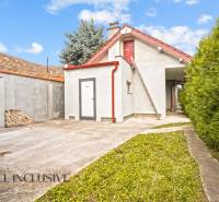 A family house in Bátorove Kosihy with a one-story extension, a gravel road, and coniferous trees.