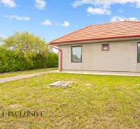 A family house in Bátorove Kosihy with a red roof surrounded by green lawn and shrubs.