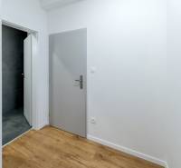 A hallway with gray doors, a bathroom with dark tiles, and a floor with a wooden decor.