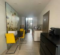 Commercial space with a dining table, yellow chairs, and a kitchenette.