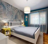 A bedroom in a family house with palm trees on the wallpaper, a wooden decor floor, and white furniture.