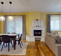 Living room with a fireplace, dining table, and wood-patterned flooring in a family house.