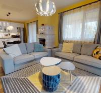 Living room in a family house with a wood-patterned floor, sofas, and a kitchen in the background.